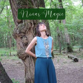 Eine Frau steht an einem Baum im Wald und trägt eine lange Kette.