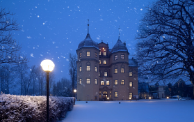Ein Schloss im Schnee umgeben von Bäumen bei Sonnenuntergang.
